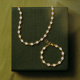 Gold-tone necklace and bracelet set with oval milky white stones, displayed on a dark olive green textured box against a matching olive green background.