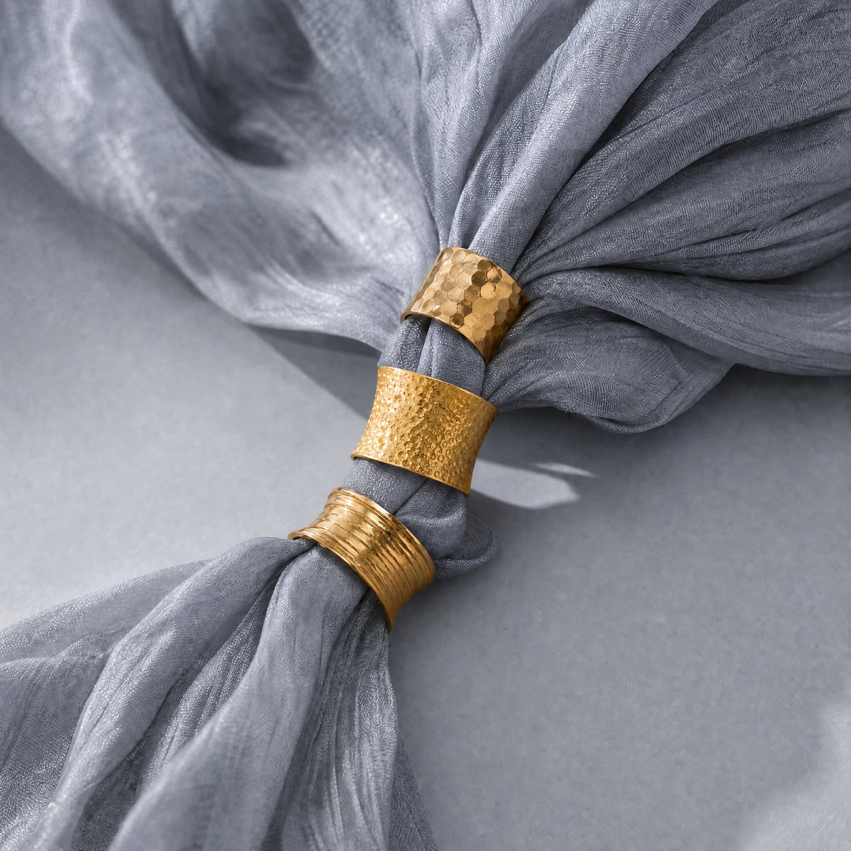 A close-up of a gray sheer fabric gathered and tied with three metallic gold bands, shown on a soft gray background.