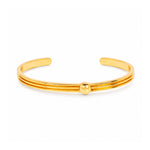 A polished gold-tone metal cuff bracelet with three parallel bands and a small central bead, shown on a clean white background.
