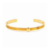 A polished gold-tone metal cuff bracelet with three parallel bands and a small central bead, shown on a clean white background.