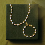 Gold-toned necklace and matching bracelet set with oval milky white stones, displayed on a dark olive green textured box against a matching olive green background.