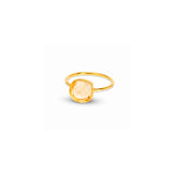 A gold ring featuring a large, cushion-cut pale peach crystal, shown on a plain white background with a soft shadow.