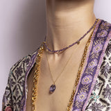 The Eva Amethyst Reversible Necklace with gold discs features handmade gold charms and vintage gemstones. Ideal for layering, this sustainable necklace illuminates in various shades of purple.
