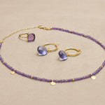 The Eva Amethyst Reversible Necklace with gold discs features handmade gold charms and vintage gemstones. Ideal for layering, this sustainable necklace illuminates in various shades of purple.